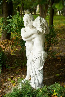 Vertical photo of marble figure of two kissing people, a boy and a girl autumn park