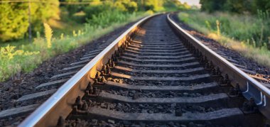 Yazın yeşil yaprakların ve güneşin arka planına karşı uzaklığa giden bir demiryolunun panoramik fotoğrafı.