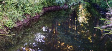Panoramic photo of rural muddy river with greenery during sunset