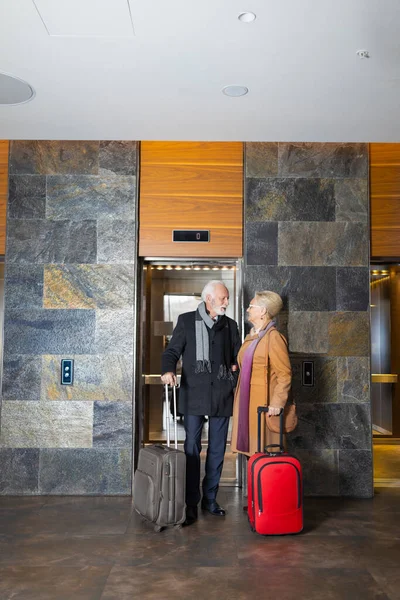 两名老年人带着手提箱站在酒店大堂 — 图库照片