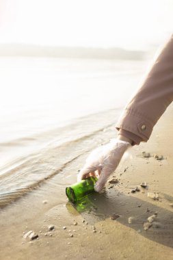 Gönüllü plajdan cam bir şişe alır.