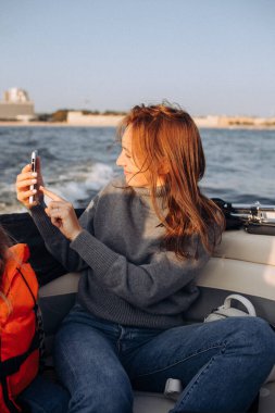 Turist kadın, sonbaharda deniz kıyısının hareketli bir fotoğrafını çekiyor. Kayıkta oturuyor, tahılla fotoğraf çekiyor.