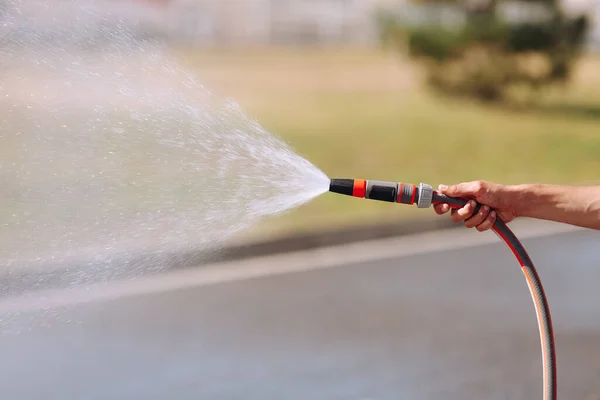 Close up of hand holding hose spraying water — Stock Photo, Image