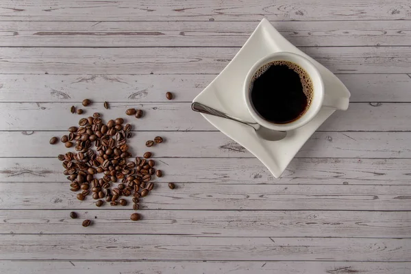 Coffee cup and coffee beans on a wooden table background laying freely