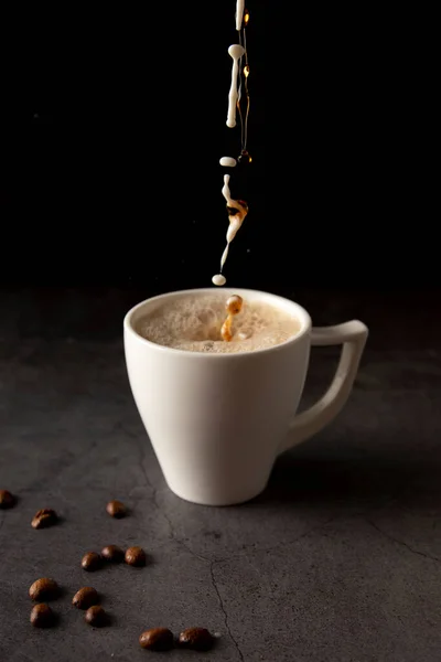 Filling a coffee cup with coffee and milk in slow motion on a concrete background