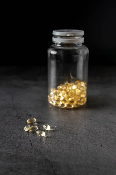 Vitamin D caps out of the container on a dark background