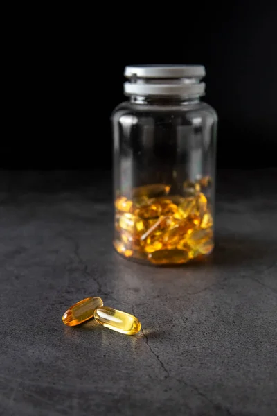 Omega 3 caps out of the container on a dark background