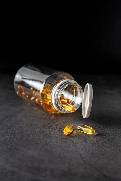 Omega 3 caps out of the container on a dark background