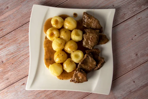 Polish traditional Stewed beef with silesian noodles and sauce on a wooden table and dark background