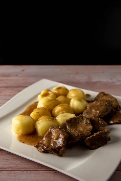 Polish traditional Stewed beef with silesian noodles and sauce on a wooden table and dark background