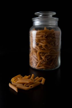 Whole grain Penne pasta in front of glass jar on the black background