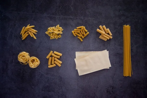 Different types of pasta including penne, fusilli, farfalle, spaghetti, lasagne, tagliatelle, papiri, tortiglioni together on a background