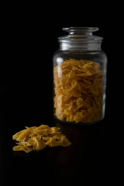 Penne pasta in front of glass jar on the black background
