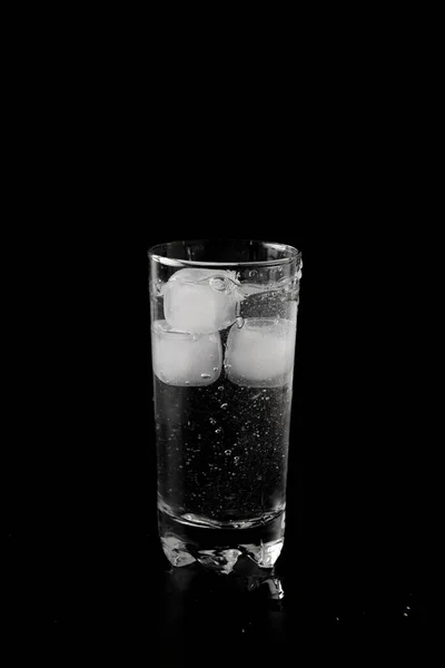 Ice cubes thrown to a glass of water from above with splash on a black background