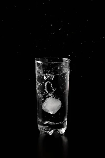 Ice cubes thrown to a glass of water from above with splash on a black background
