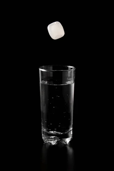 Ice cubes thrown to a glass of water from above with splash on a black background