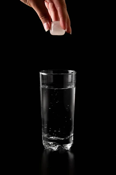 Ice cubes thrown to a glass of water from above with splash on a black background