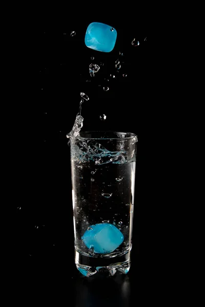 Colour Ice cubes thrown to a glass of water from above with splash on a black background