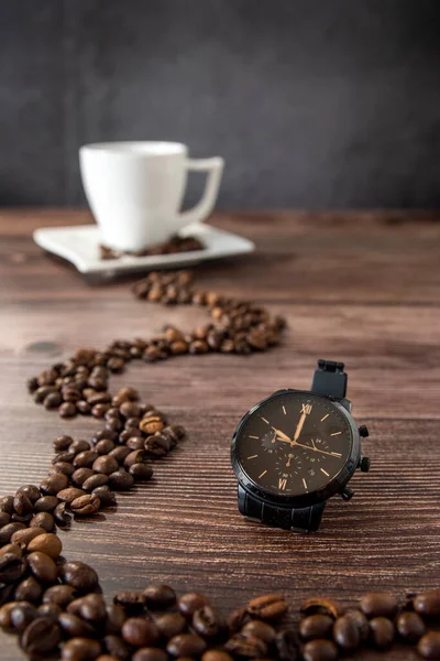 Watch showing best time for coffee with cup of coffee in the background on the wooden table