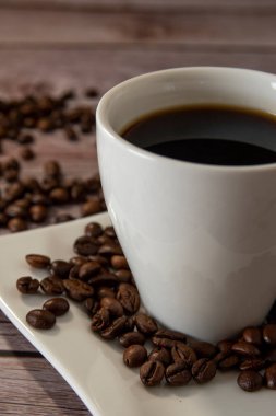 Cup of coffee on a light wooden table with coffee beans and dark background