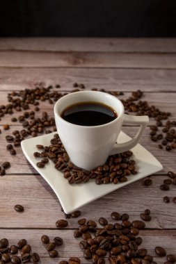 Cup of coffee on a light wooden table with coffee beans and dark background