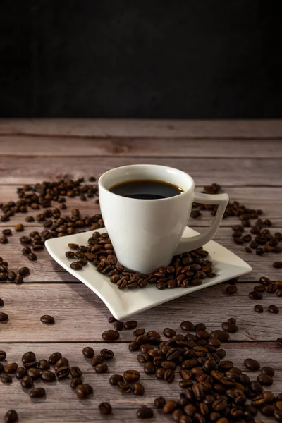 Cup of coffee on a light wooden table with coffee beans and dark background