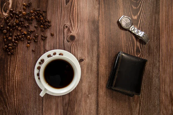 Coffee cup on a wooden table with wallet and watch from above