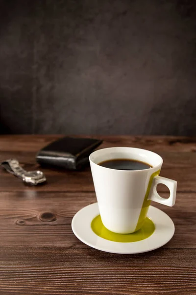 Coffee cup on a wooden table with wallet and watch