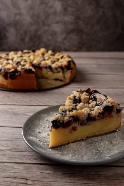 Piece of blueberry cake on wooden table with sugar powder