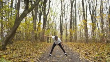Yeşil kulaklıklı bir sporcu parkta müzik dinler ve koşmadan önce ısınır. Spor ve sağlık