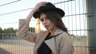 Güzel kız model sokakta durur ve bir şapka takar. Siyah şapkalı, kahverengi pelerinli, uzun saçlı esmer kadın. Arkadan portre çerçevesi