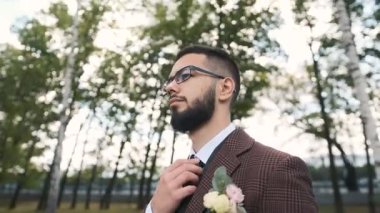 Gözlüklü ve şık kahverengi takım elbiseli vahşi beyaz adam parkta yürüyor kravatını düzeltiyor ve bir iş planı düşünüyor.