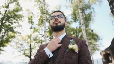 Gözlüklü ve şık kahverengi takım elbiseli vahşi beyaz adam parkta yürüyor kravatını düzeltiyor ve bir iş planı düşünüyor.