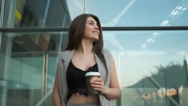 Caucasian woman with long hair walks near offices and enjoys coffee — Vídeo de stock