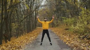 Bearded man of Caucasian appearance in yellow clothes warms up in the park