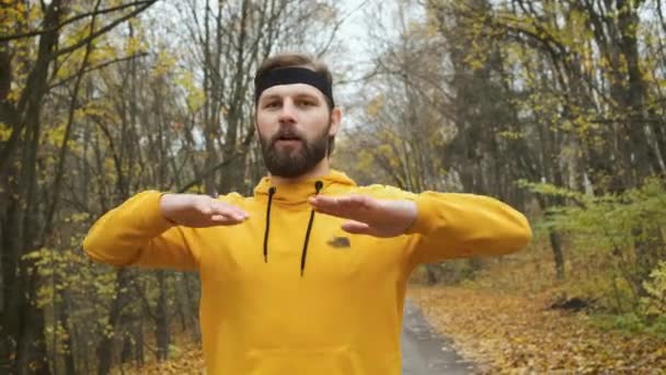 Brodaty mężczyzna o wyglądzie kaukaskim w żółtych ubraniach rozgrzewa się w parku — Wideo stockowe