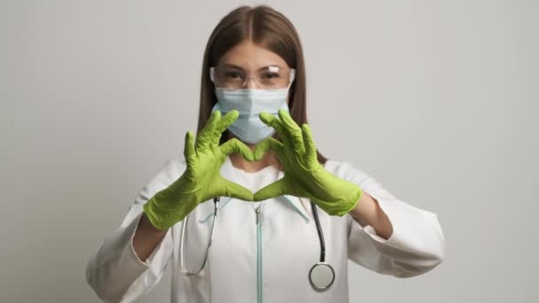 Воненний лікар в рукавичках і стетоскоп, що показує форму серця, дивлячись на камеру — стокове відео