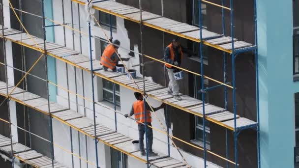 Craftsmen on the scaffolding on the construction site make the facade — Stock videók