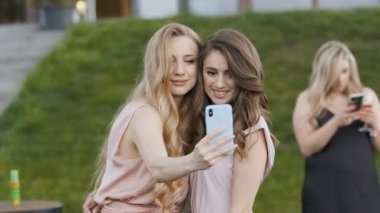 Sarışın ve esmer elbiseli iki güzel beyaz kadın bir partide selfie çekiyorlar..