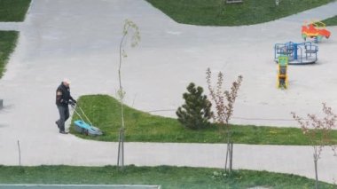 Bir adam çim biçme makinesiyle çimleri biçiyor. Çimen ve çocuk parkı bakımı.