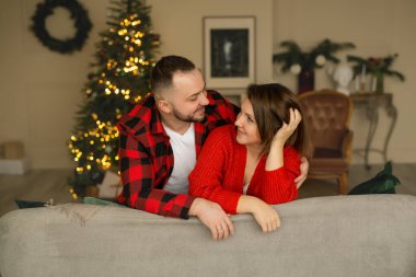 Kucaklaşan genç ve güzel bir çift bir Noel ağacının arka planında birbirlerine sevgiyle bakar. Yeni yıl arifesinde aşıklar. Noel süslemeleri olan rahat bir oda.