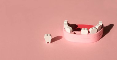 Pembe stüdyo arka planında dişi eksik bir insan çenesinin tahta maket oyuncağı. Diş dökülmesi sorunu. Süt dişleri. Pankart. Boşluğu kopyala.