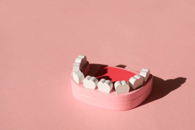 Diş fırçalama ve diş bakımı yapan bir dişçi tarafından klinik hastalarına sunulan tahta bir çene modeli. Pembe arka planda izole edilmiş, gölgeli. Diş konsepti. Yakın çekim