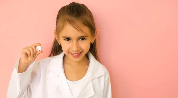 白い医療用のコートに医者を描いた陽気な女の子は手に歯を持っています 歯の概念 自然の健康的で強い雪の白い歯 歯科治療と衛生 バナーだ スペースのコピー — ストック写真