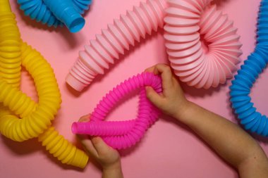 Bir çocuk stres önleyici bir pop melodisi oyuncağını elinde tutuyor. Farklı boylarda ve renklerde oyuncaklar pembe bir arka planda düğümlenmiş..