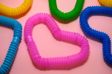 Çok renkli pop tüpleri, kalp şeklinde birbirine bağlıdır. Pembe bir stüdyo arka planında izole edilmiştir..