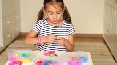 Beş yaşındaki bir kız lastik bantlardan aksesuar dokumakla meşgul. Bir takım dokuma aletleri ve çocuğun önündeki masada duran plastik kaplarda renkli lastikler. Çocuk hobileri