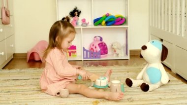 Bir kız çocuk odasında çay partisinde peluş bir köpekle bulaşıklarla oynuyor. Çocuk bir arkadaşının ikramı için pastayı parçalara ayırır. Şenlik masası için tahta oyuncaklar.