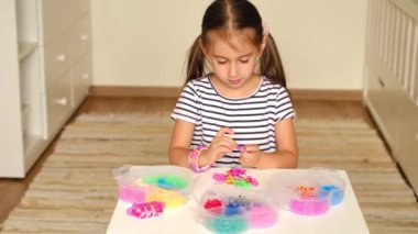 Beş yaşındaki bir çocuk lastik bantlarla örgü örüyor. Bir takım dokuma aletleri ve kalp şeklinde plastik kaplarda renkli bir kauçuk. Hobiler ve eğlence