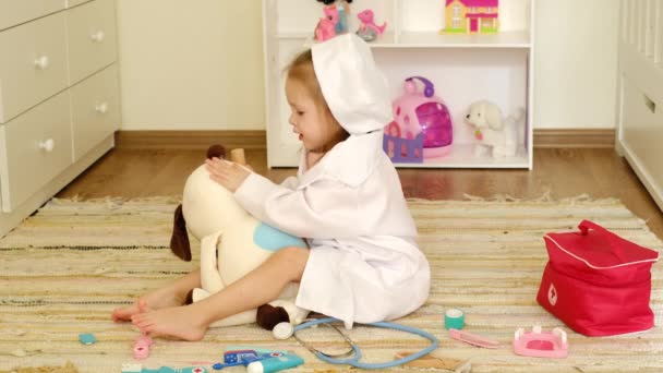 身着医用长袍的婴儿在毛绒玩具狗身上涂上治疗药膏 扮演兽医的角色 在地板上的儿童房里玩玩具的医生 — 图库视频影像